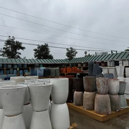 Outdoor display of various large ceramic pots and planters under overcast sky in a garden center