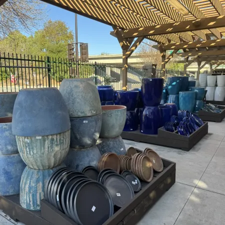 Outdoor display of various ceramic pots and trays under a wooden pergola on a sunny day.