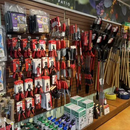 Wall display of gardening tools including pruners, clippers, hand trowels, shovels, and garden supplies in a store.