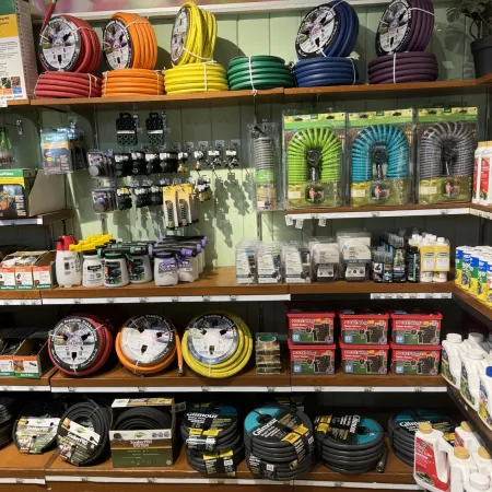 Shelves displaying colorful garden hoses, hose accessories, sprayers, and gardening products in a store.