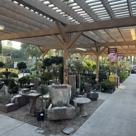 Outdoor garden center with wooden pergola displaying fountains, plants, and garden decor along concrete pathways.