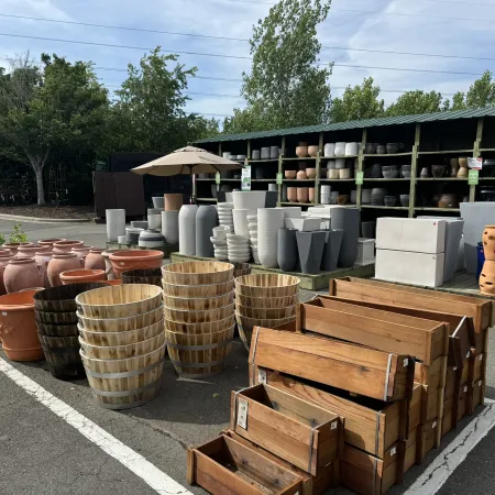 Outdoor display of various empty garden pots, wooden planters, and ceramic containers under blue sky.