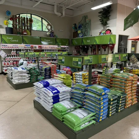 Garden supply store aisle with bags of soil, fertilizers, insect control, disease control, and gardening tools.