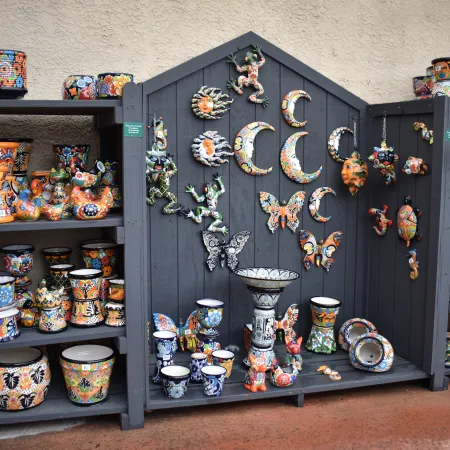 Colorful Talavera pottery and wall decorations displayed on dark wooden shelves and panels indoors.