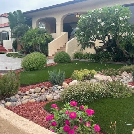 Front yard with manicured landscaping featuring green shrubs, flowering plants, rocks, and mulch in a residential area.