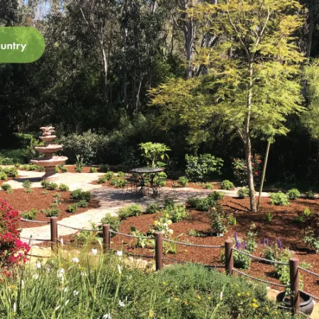 Italian country garden with vibrant flowers, stone pathways, fountain, and lush greenery under sunlight.