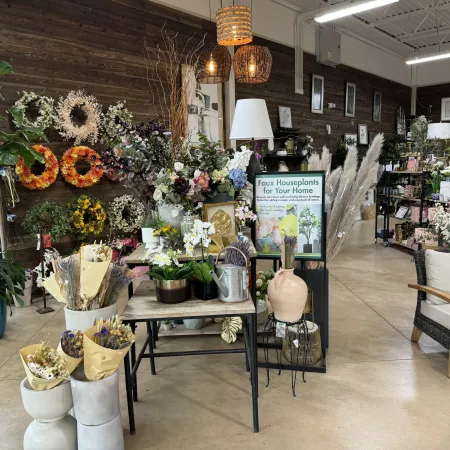Interior view of a floral shop with artificial flowers, wreaths, potted plants, and decorative home items