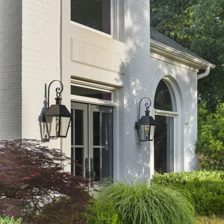 Modern white brick house entrance with black doors, lantern lights, and lush green landscaping with rocks.