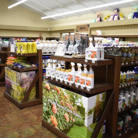 Gardening store interior with shelves displaying fertilizers, plant food, tools, and garden supplies under bright lights.