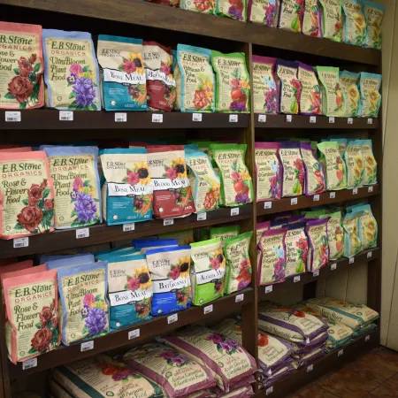Shelf displays multiple colorful packets of E.R. Stone Flower Power organic gardening products with floral designs.