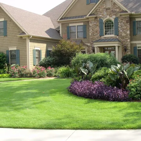 Large suburban house with stone and siding exterior surrounded by lush green lawn and colorful garden beds