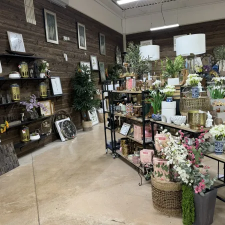 Interior of a rustic gift shop with shelves displaying clocks, vases, flowers, and decorative items on a polished floor.