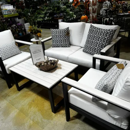 Modern outdoor seating group with white cushions, patterned pillows, and a wooden coffee table in a store setting