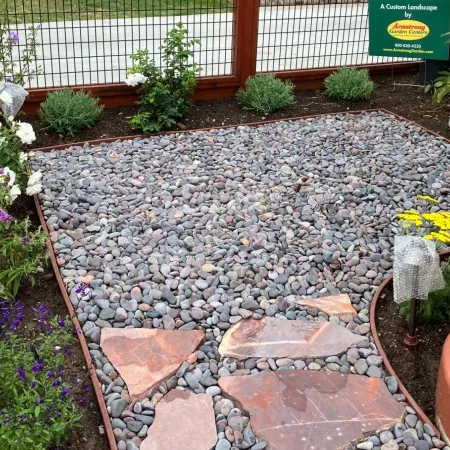 Curved garden pathway made of small river rocks with large flat stones and surrounding plants in mulch beds.