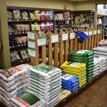 Bags of fertilizer and soil products stacked neatly inside a farm supply store with hats hanging on the wall.