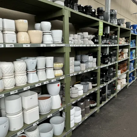 Shelves filled with various ceramic and plastic plant pots in different shapes and colors in a store aisle.