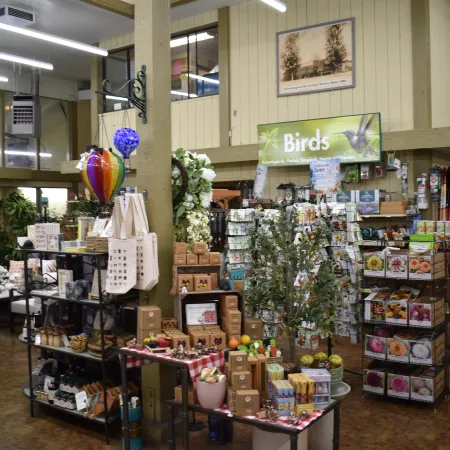 Garden store interior with plants, gardening tools, bird supplies, and decorative items on display.