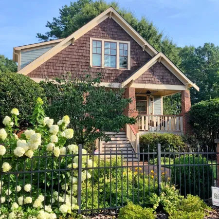 Charming craftsman-style house with brown shingles, front porch, white hydrangeas, and black iron fence on a sunny day