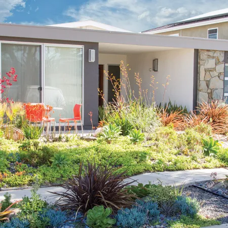 Modern house with a drought-tolerant garden featuring succulents and a patio with orange chairs under a covered porch.