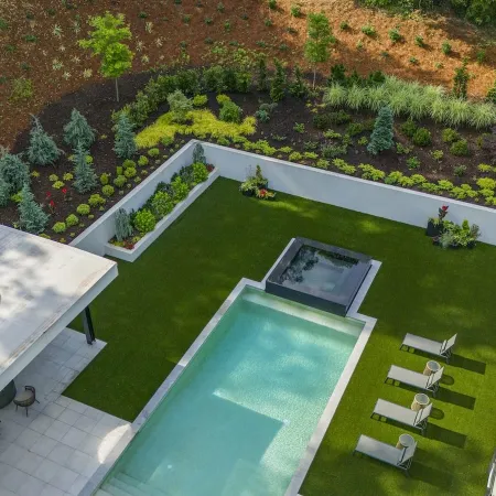 Aerial view of modern backyard with rectangular pool, hot tub, lawn chairs, and landscaped garden beds.