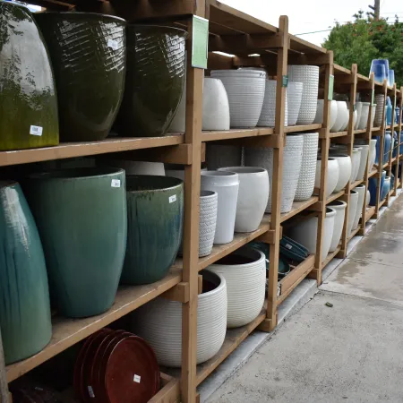 Outdoor shelves filled with various large ceramic and plastic garden pots in different colors and sizes.