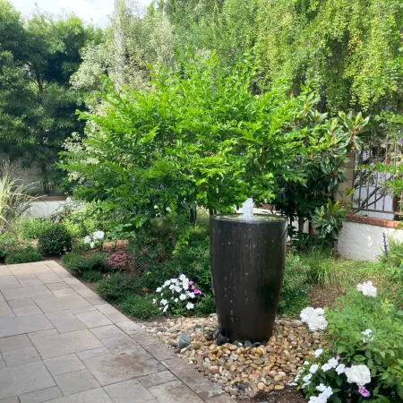 Tranquil garden with a tall black water fountain surrounded by lush greenery and blooming flowers.