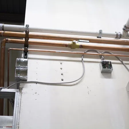 Copper and PVC pipes installed along a white wall with metal electrical conduits and junction boxes for building utilities.
