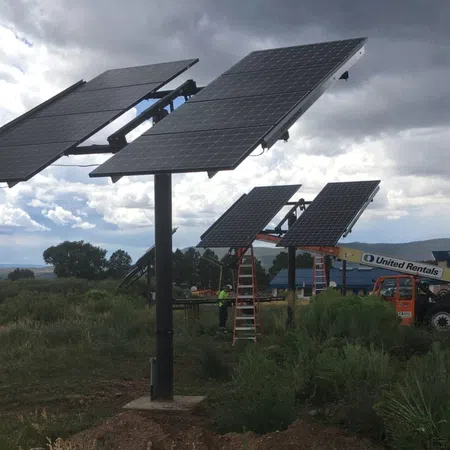 Solar panels mounted on poles in a field with workers and equipment under a cloudy sky.
