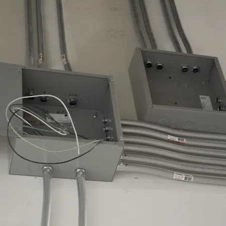 Open electrical junction boxes with metal conduit and wiring installed on a wall during construction.