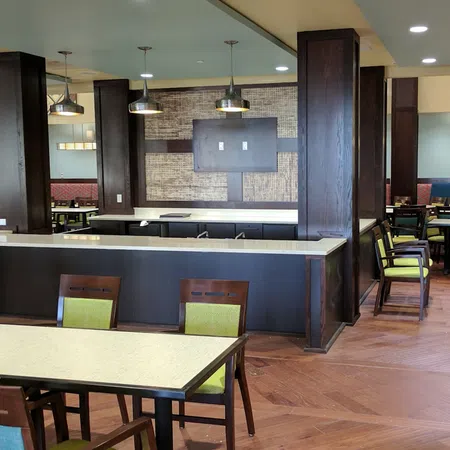 Modern dining area with wooden tables and chairs featuring green cushions and pendant lighting in a spacious room.