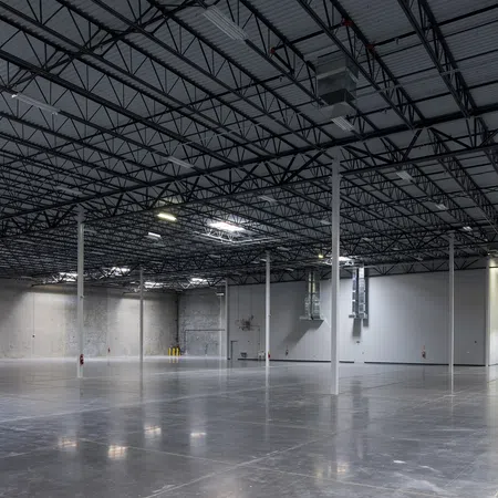 Spacious empty industrial warehouse with polished concrete floor and high ceiling with metal beams and columns.