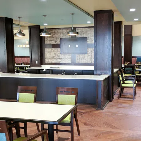 Modern dining area with wooden tables, green and blue cushioned chairs, pendant lights, and hardwood flooring.