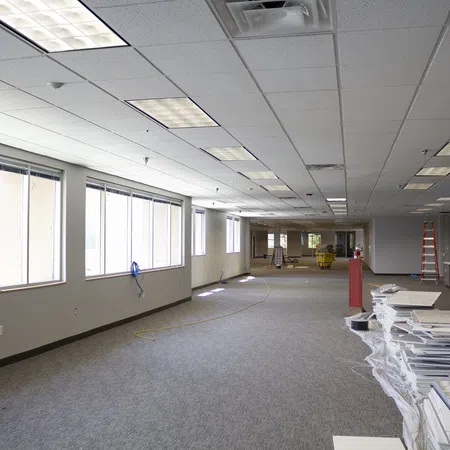 Spacious office interior under renovation with carpet flooring, ceiling lights, and construction materials.