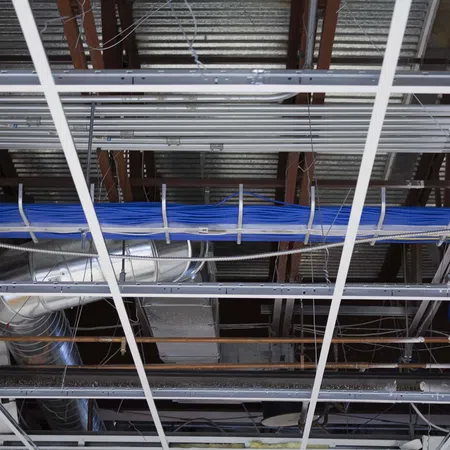 Exposed industrial ceiling with metal ducts, blue electrical cables, and grid framework in a commercial building.