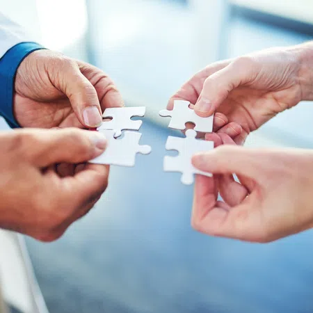 Four hands holding white puzzle pieces about to connect symbolizing teamwork and collaboration