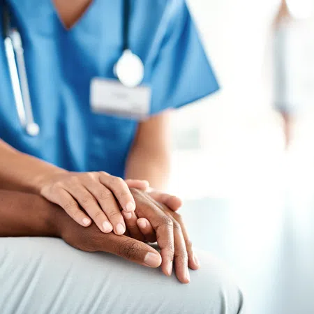 Healthcare professional in blue scrubs comforting patient by holding their hand in a medical setting.