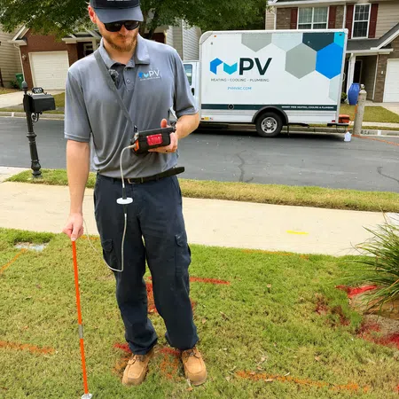 Technician wearing PV HVAC uniform using equipment to measure gas or pressure outside a residential home.