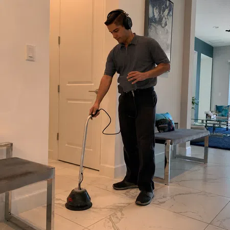 Man using a floor polishing machine on marble tiles in a modern living room.