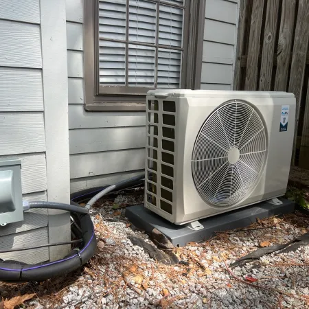 Outdoor HVAC unit installed on gravel next to house siding and wooden fence under sunlight.