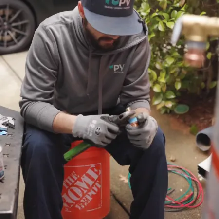 A technician installs a heat pump water heater outdoors with tools in hand.
