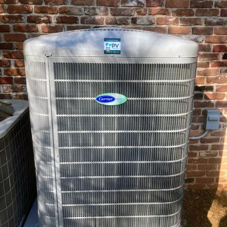 Carrier air conditioning unit against a brick wall, showcasing modern HVAC technology in residential setting.