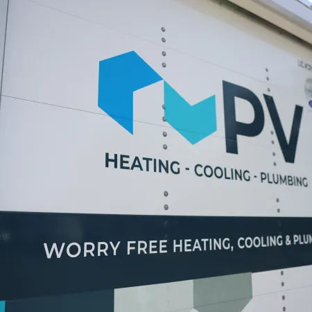 PV Heating Cooling Plumbing logo and slogan on a white service vehicle door with outdoor background.