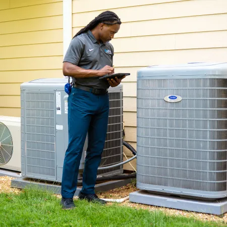 Technician inspecting and documenting the condition of three outdoor air conditioning units beside a house.