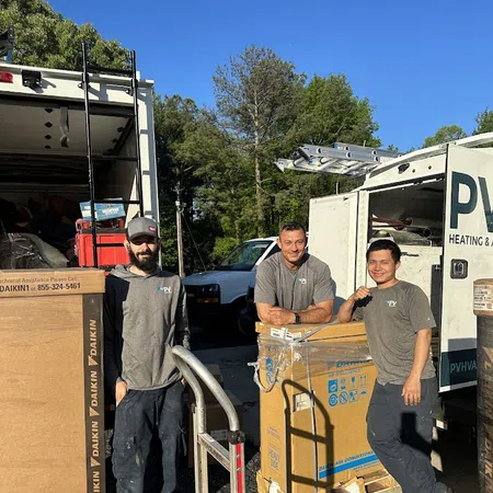 Three HVAC technicians standing by delivery trucks with Daikin air conditioning units outdoors on a sunny day.