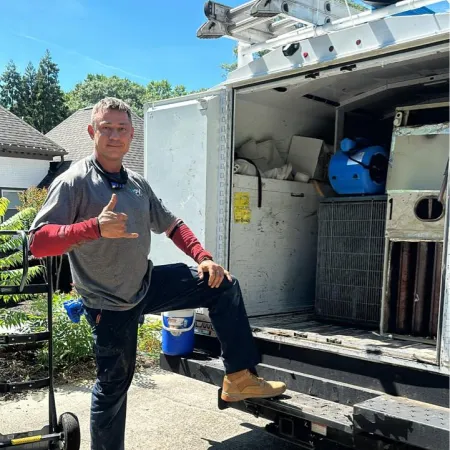 Man in workwear posing with hand gesture next to open work truck loaded with tools and equipment.