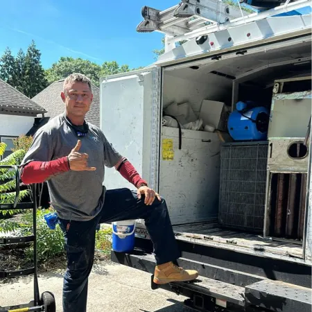 Man in workwear posing with hand gesture next to open work truck loaded with tools and equipment.