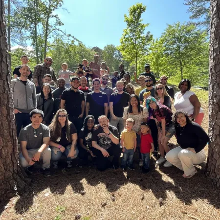 Large diverse group of people posing outdoors between two trees on a sunny day in a forested area