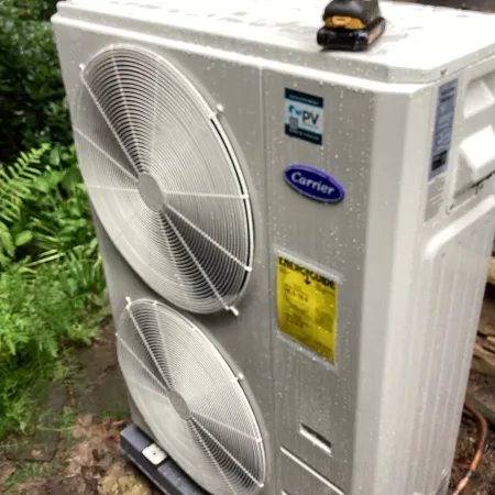 Carrier outdoor air conditioning unit with dual fans, installed in a lush outdoor setting.