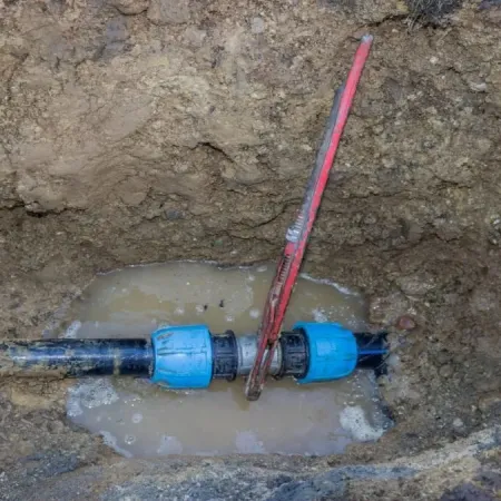 Exposed underground water pipe with valve and muddy water in a trench during repair work.