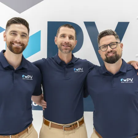 Three men in navy blue PV polo shirts posing and smiling in front of a PV branded background